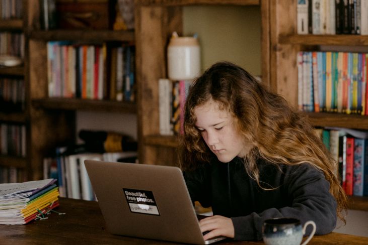 A teenager sitting at a laptop in front of bookshelves.