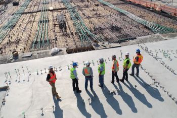 Construction workers standing on a concrete area next to a construction site.