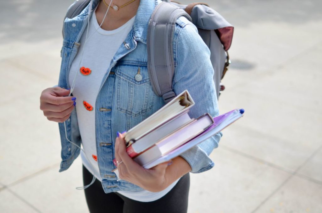 Student with a backpack on carrying a stack of books.
