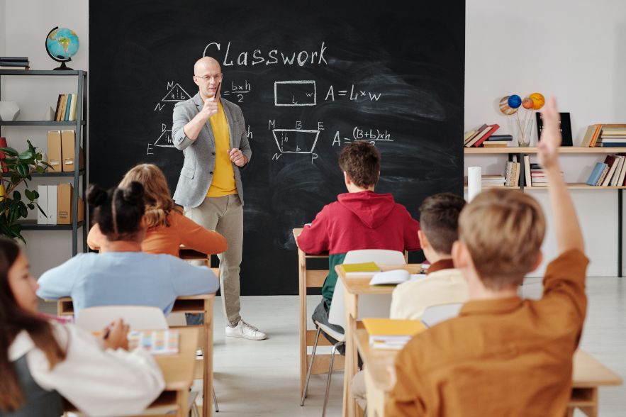 Teacher standing at a blackboard in front of a class of students.