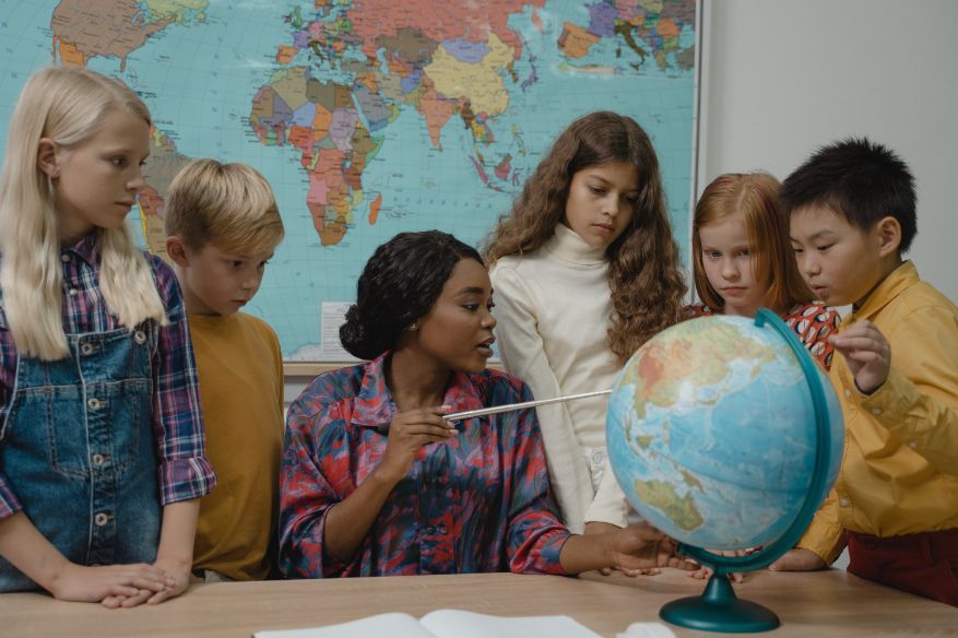 Students gathered around a teacher pointing at a globe.